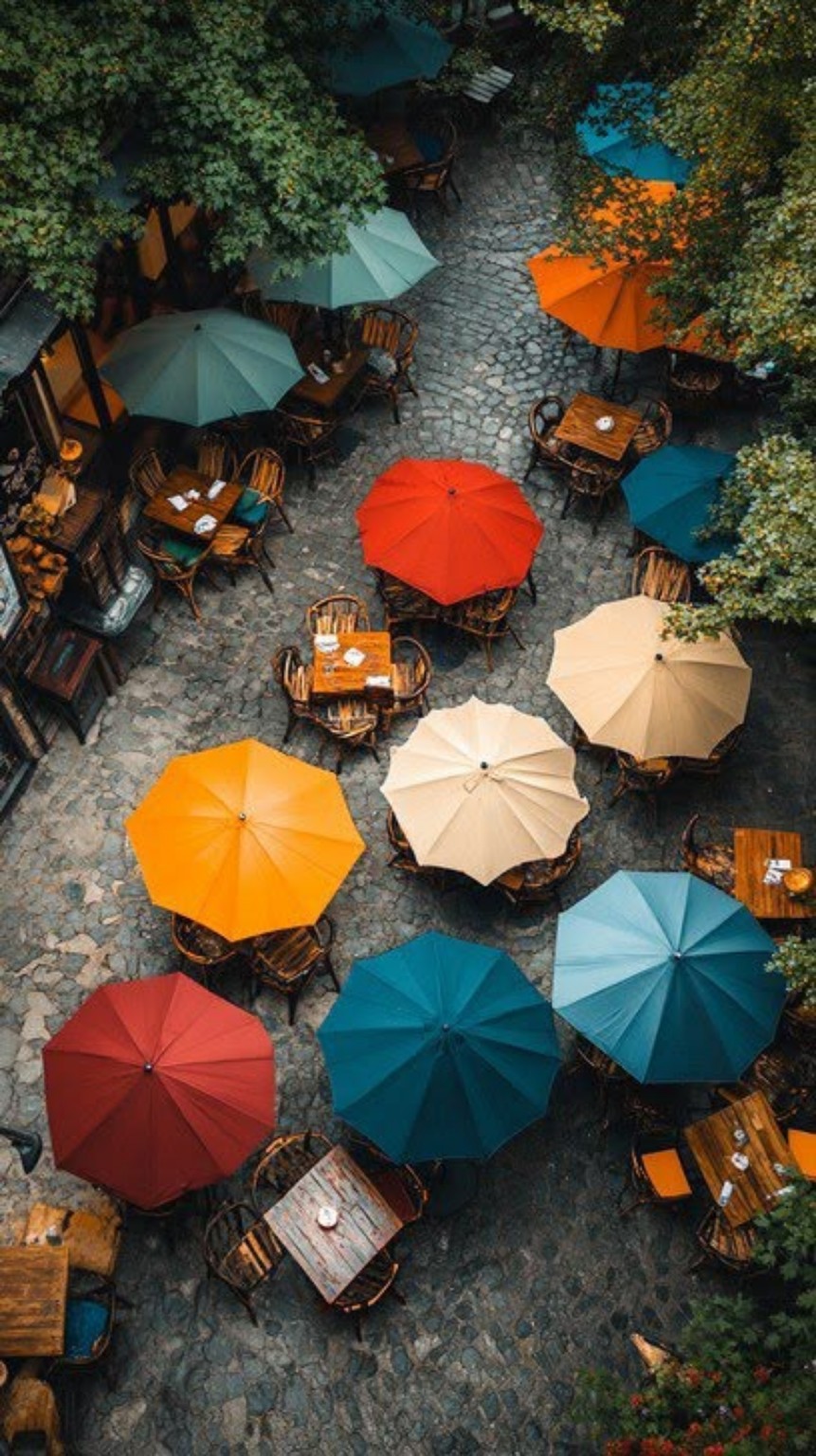 Une terrasse pavée vue du ciel, avec des parasols orange, jaunes, rouges et bleus.