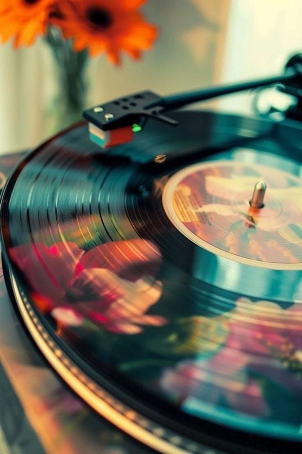 Un disque vinyle sur une platine, avec des reflets turquoise et des fleurs orange en arrière-plan.