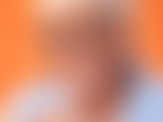 Retrato de Dona Maria, mulher negra de 78 anos. Ela está sorrindo, usa óculos com aro marrom, está vestindo uma faixa bege na cabeça escondendo os cabelos e usa uma blusa azul clara. A mão, dobrada à frente do colo, está com as unhas pintadas de vermelho e o fundo é uma parede laranja.