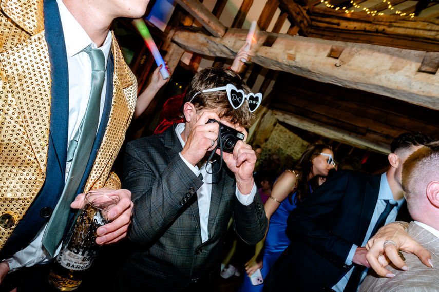 Wedding guest in heart glasses filming at a lively reception