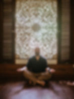 Man meditating in front of an ornate screen