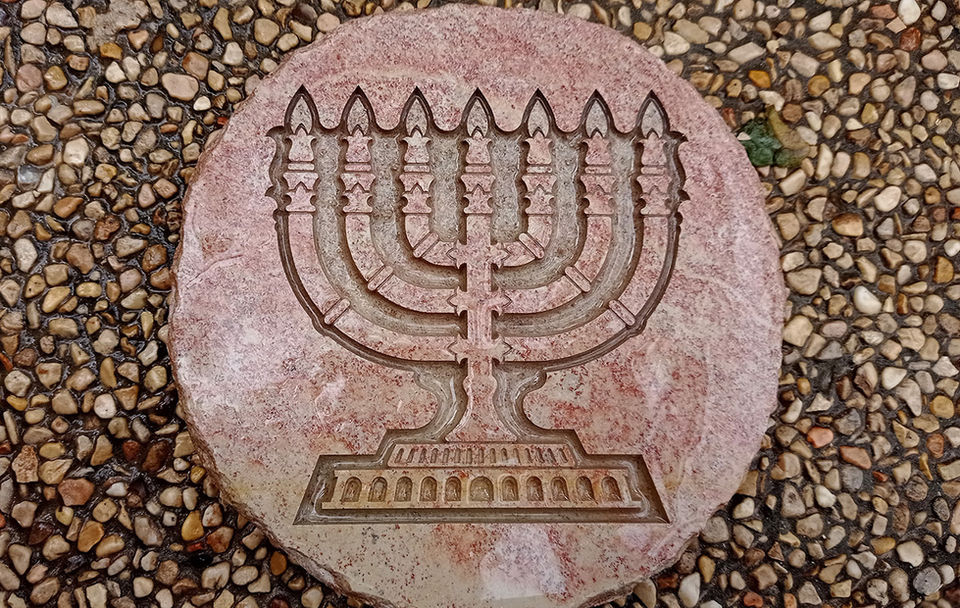 Round Jerusalem stone plaque engraved with a seven-branched menorah, photographed on pebble ground