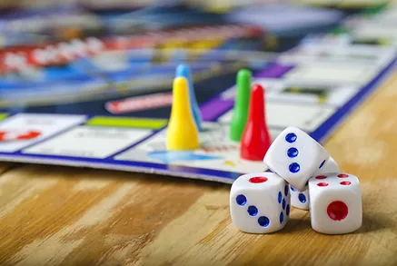 Pcture of a board game with placer pieces (yellow, red, green, and blue). in the forefront are a pile of dice
