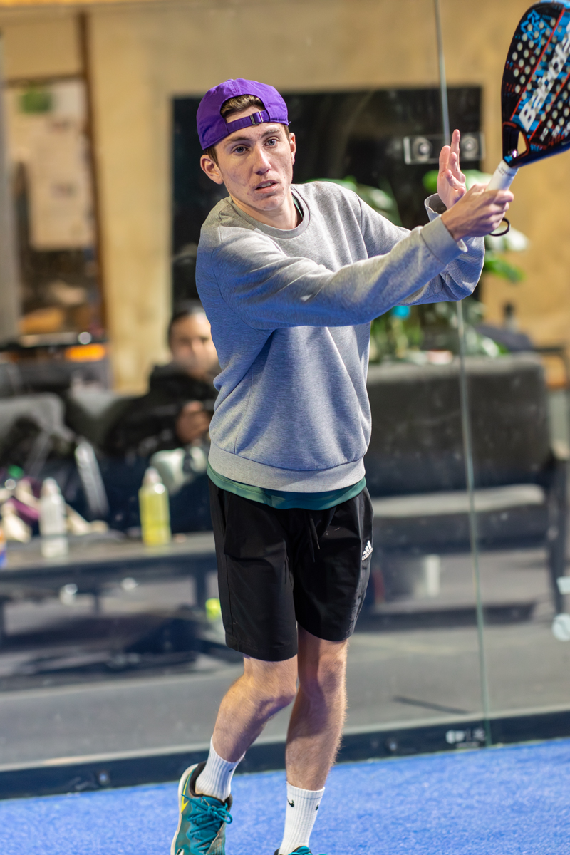 Padelspieler in Aktion, bereit zum Schlagen, mit Schläger und Sportkleidung.