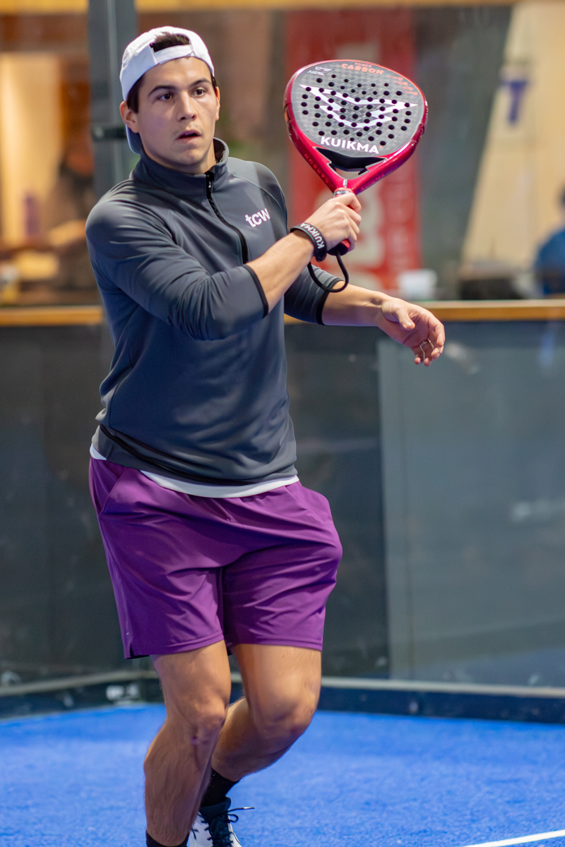 Ein junger Mann spielt Padel Tennis mit rotem Schläger im Innenbereich.