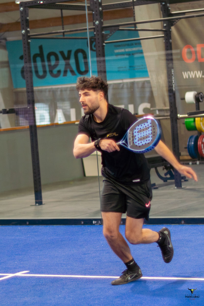 Athletischer Mann spielt Padel, adexos Logo, auf blauem Indoor-Platz.