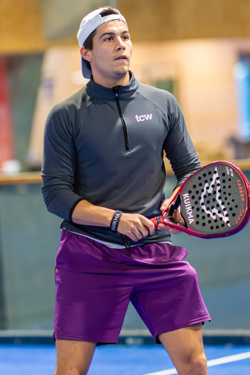 Padelspieler mit Schläger und Sportkleidung auf dem Platz, bereit zum Spiel.