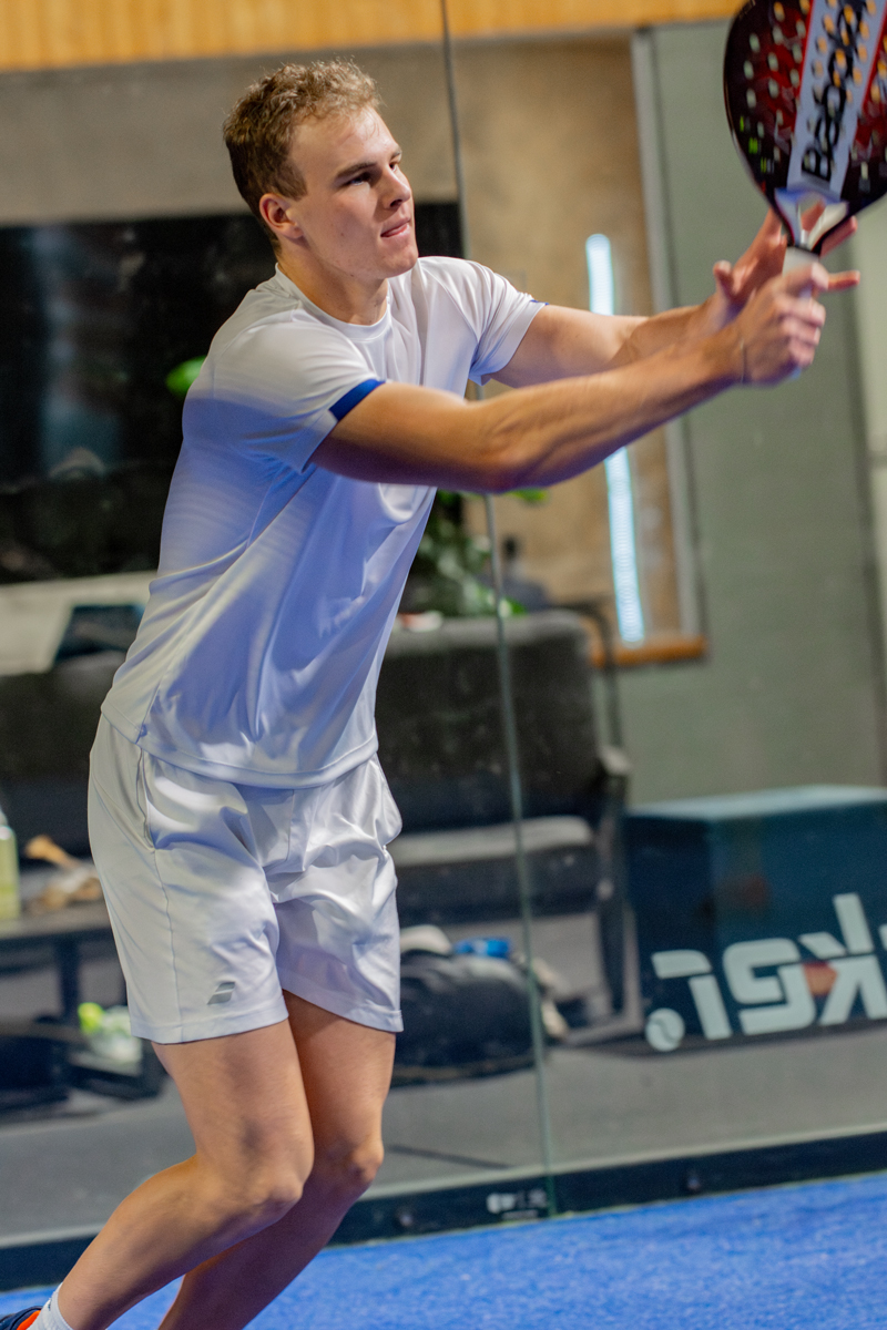 Ein junger Mann beim Padel-Tennis schlägt den Ball, Konzentration im Gesicht.