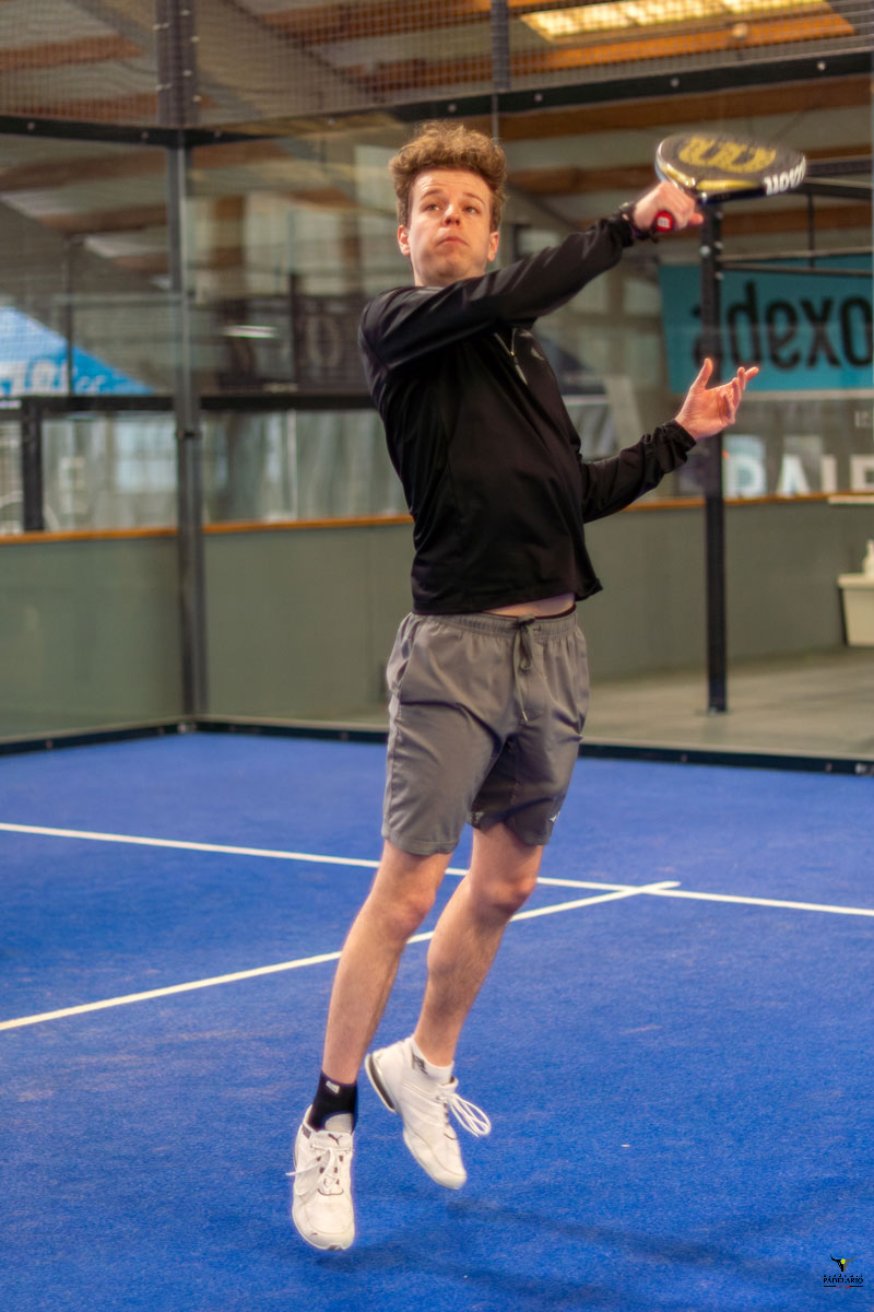 Junger Mann springt auf blauem Padelplatz mit Schläger bereit zu schlagen. "dexco" im Hintergrund.