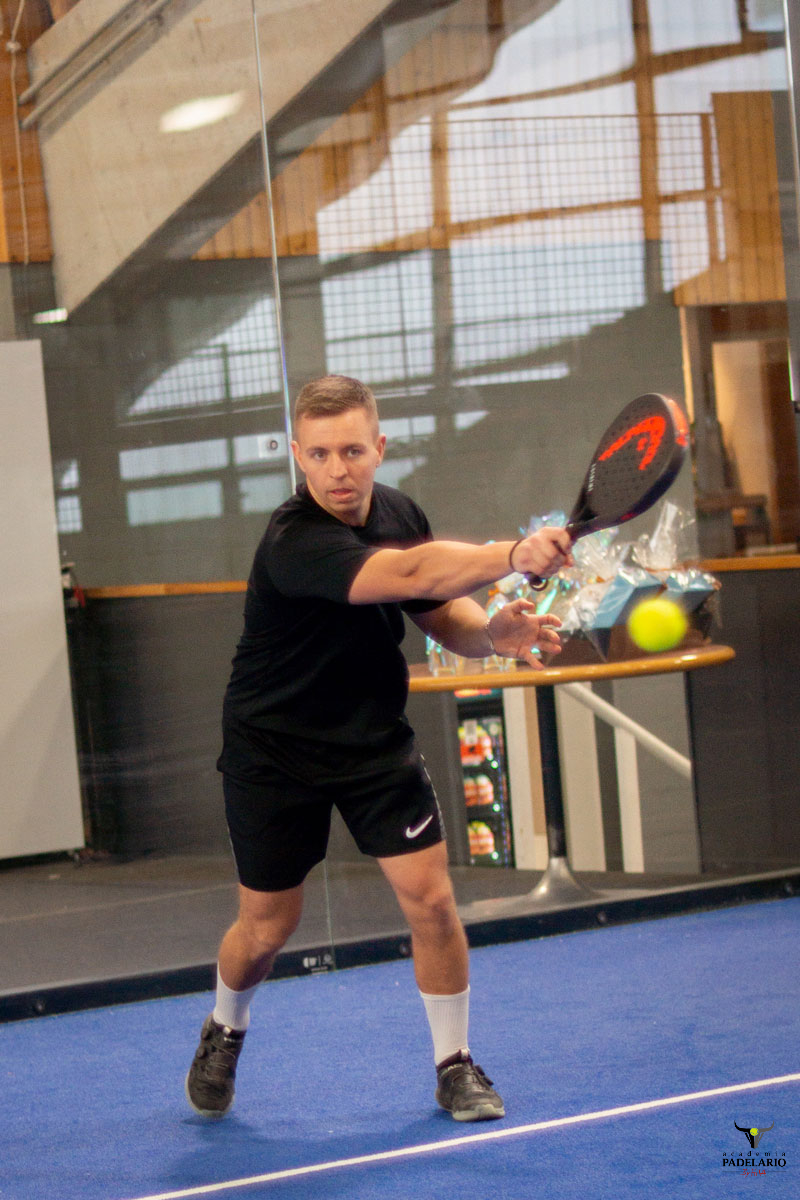 Fokussierter Mann spielt Padel, schwingt Schläger auf blauem Padelplatz.