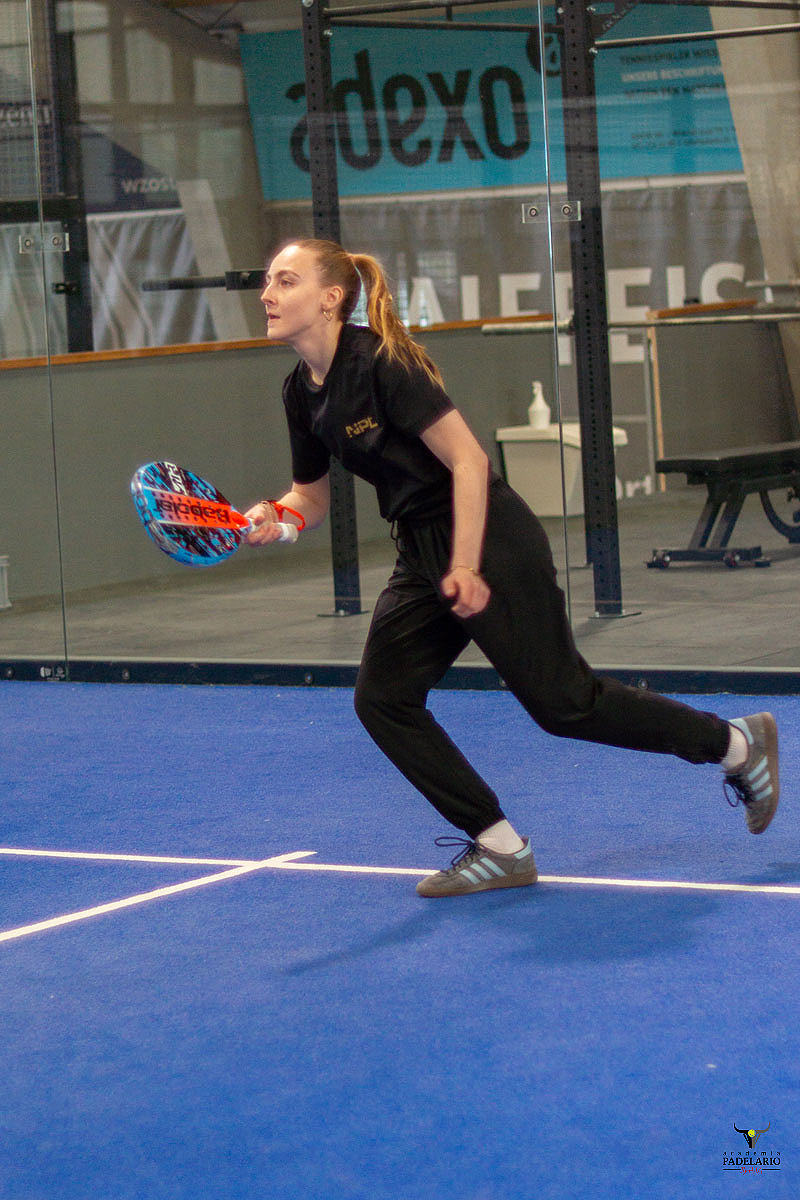 Junge Frau spielt Padel mit Adexo im Hintergrund auf blauem Padelplatz.