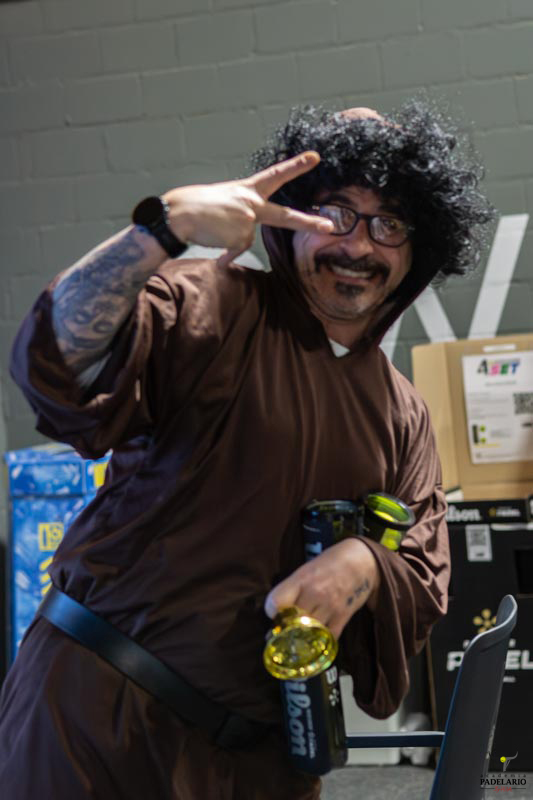 Mann in Mönchskostüm mit Peace-Zeichen und Getränk auf Event.