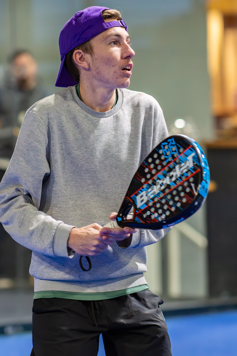 Junge Mann mit lila Mütze beim Padel-Tennisspiel, Babolat Schläger haltend