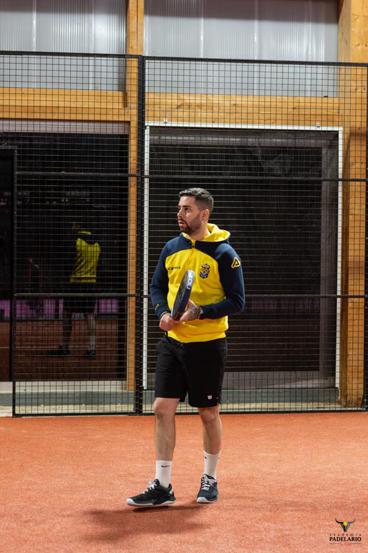 Mann mit Schläger auf dem Platz, in einem gelben Hoodie, Turnier vorbereitet.