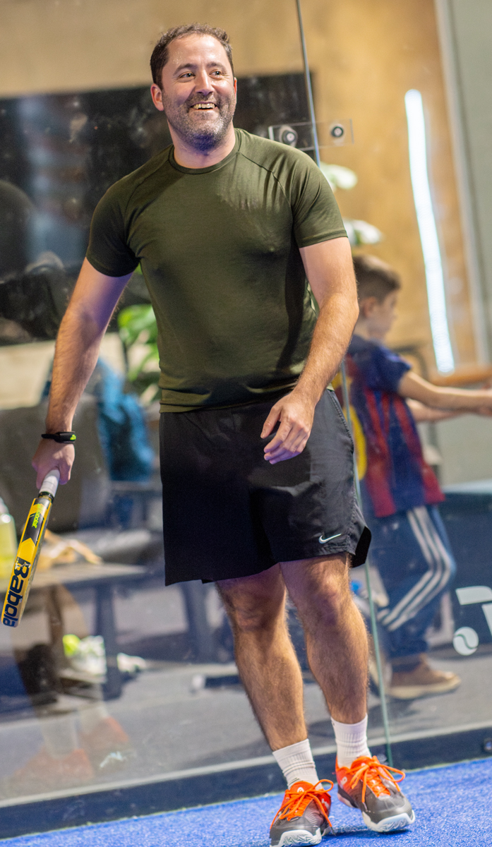 Mann lächelt und spielt Padel, trägt Sportkleidung und hält Schläger in der Hand.
