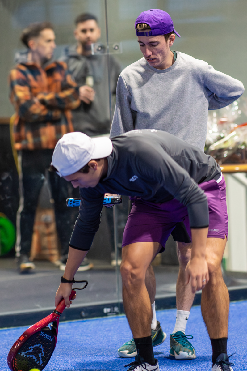 Zwei Männer spielen Padel und einer zeigt dem anderen etwas auf dem Platz.