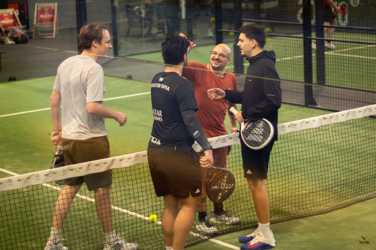 Vier Männer unterhalten sich auf einem Padelplatz neben dem Netz.