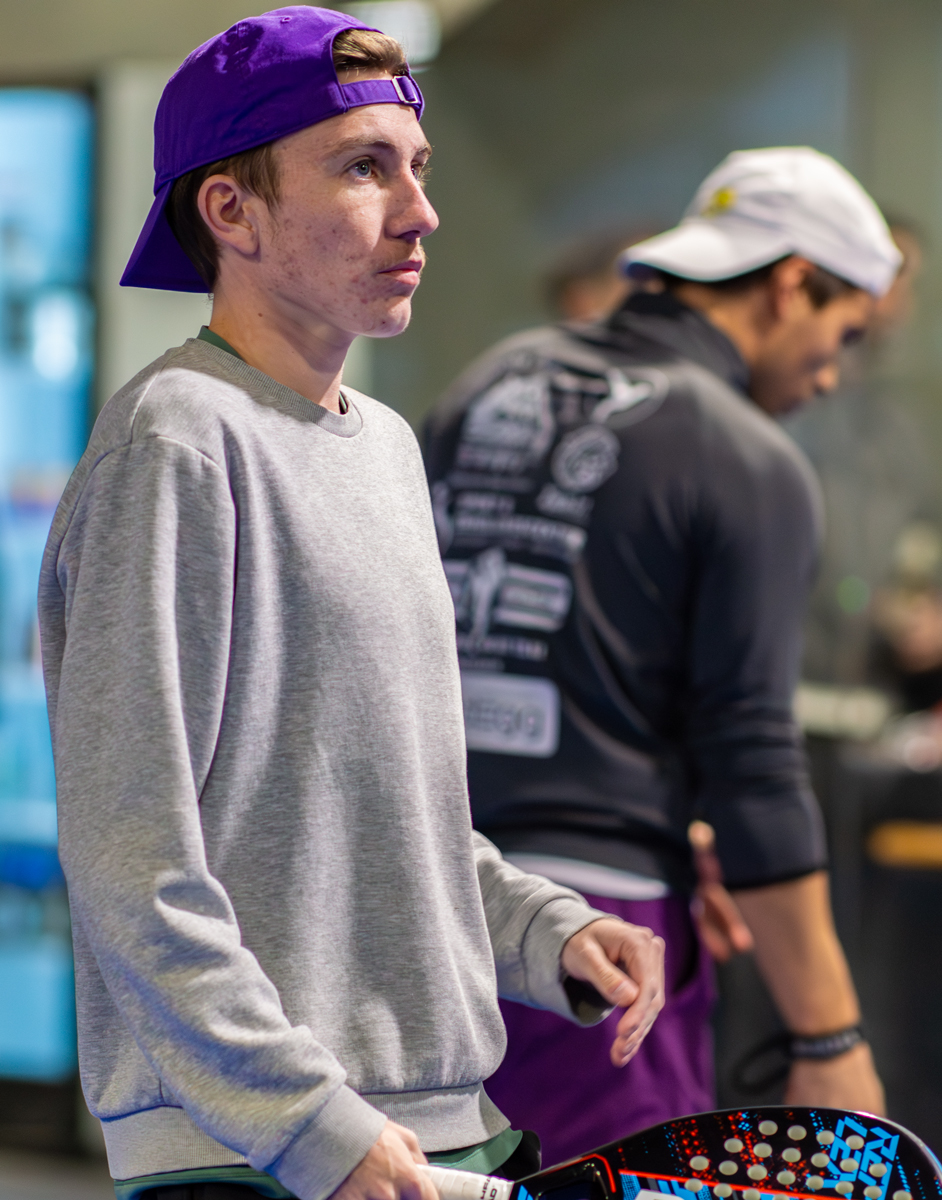 Ein junger Mann mit lila Mütze, Turnier 30-11-25, konzentriert beim Tennisspielen.