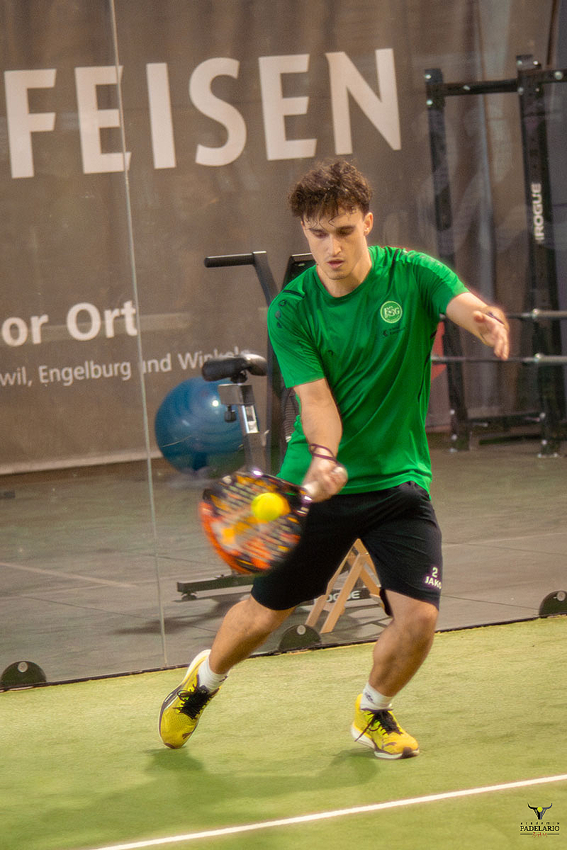 Junger Padelspieler schlägt Ball mit Padel-Schläger vor "FEISEN" Wand.