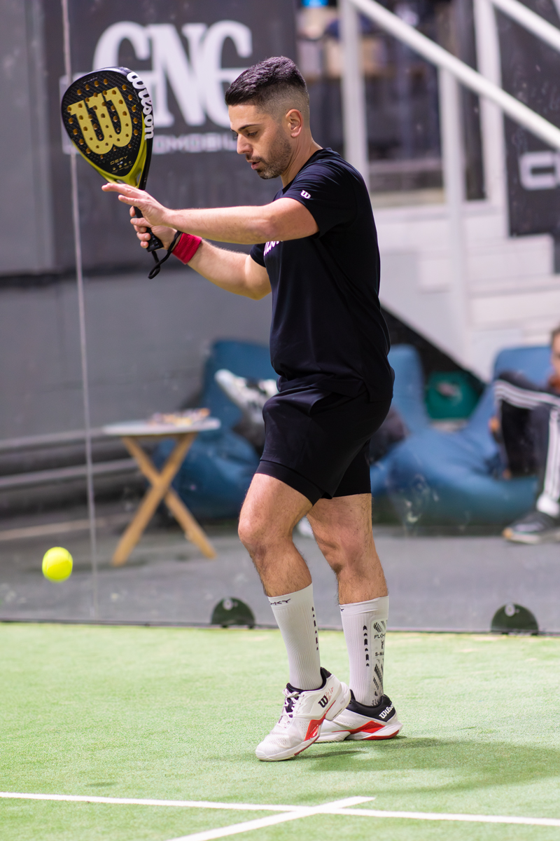 Mann schlägt Ball mit Schläger, Text auf Schläger und Hintergrund ist sichtbar.