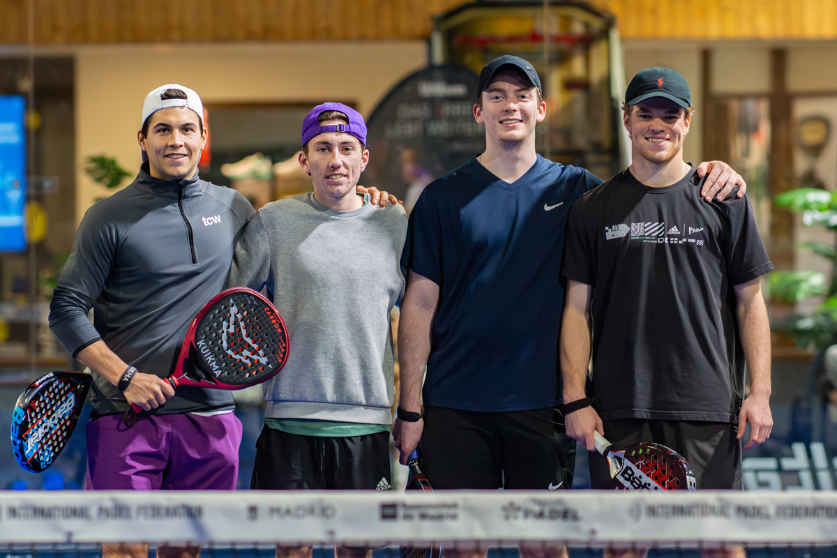 Four padel players pose smiling behind a net holding rackets in Madrid, Spain.