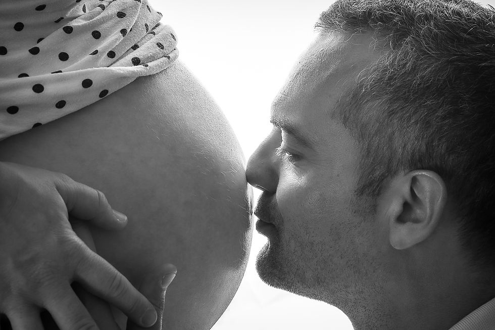 Homme en noir et blanc embrassant le ventre d’une femme enceinte, main posée dessus, gros plan tendre.