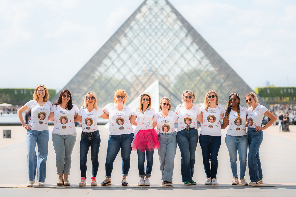 Groupe de femmes posant devant la pyramide du Louvre, portant des t-shirts. photographe