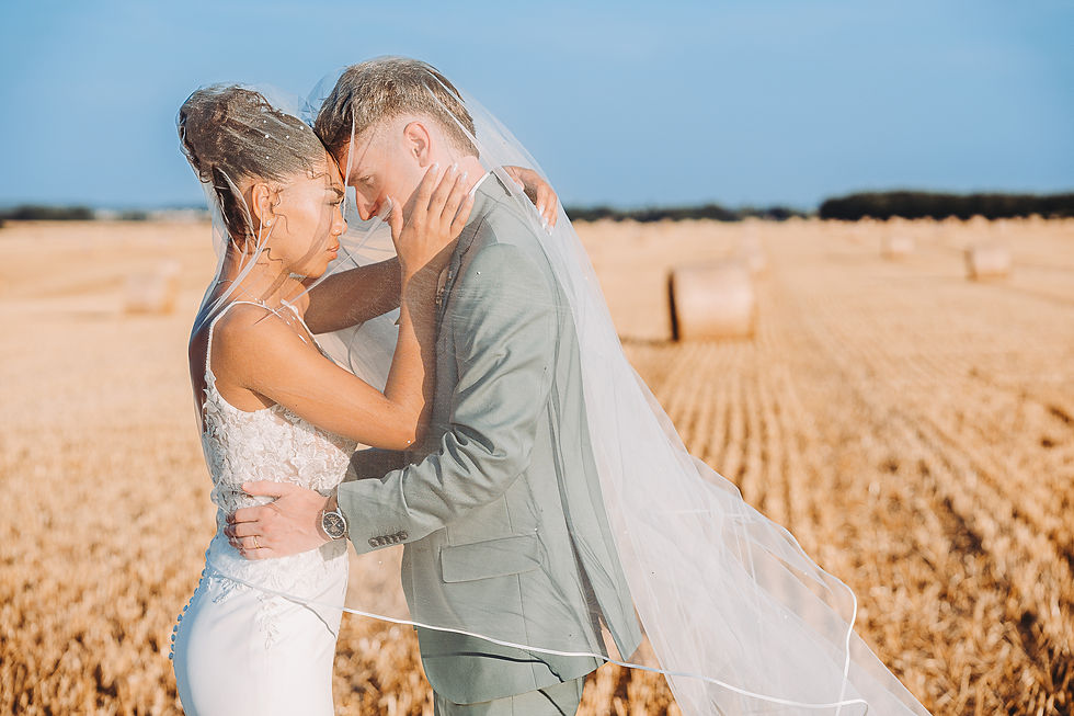 Mariés enlacés sous un voile blanc dans un champ de blé doré, front contre front, ambiance romantique.