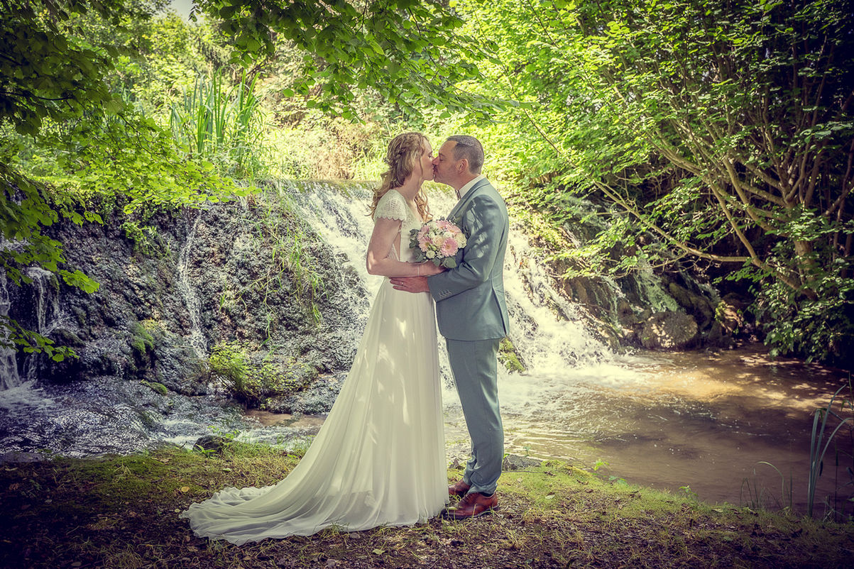 Couple s'embrassant devant une cascade, mariage, robe blanche, heureux photographe