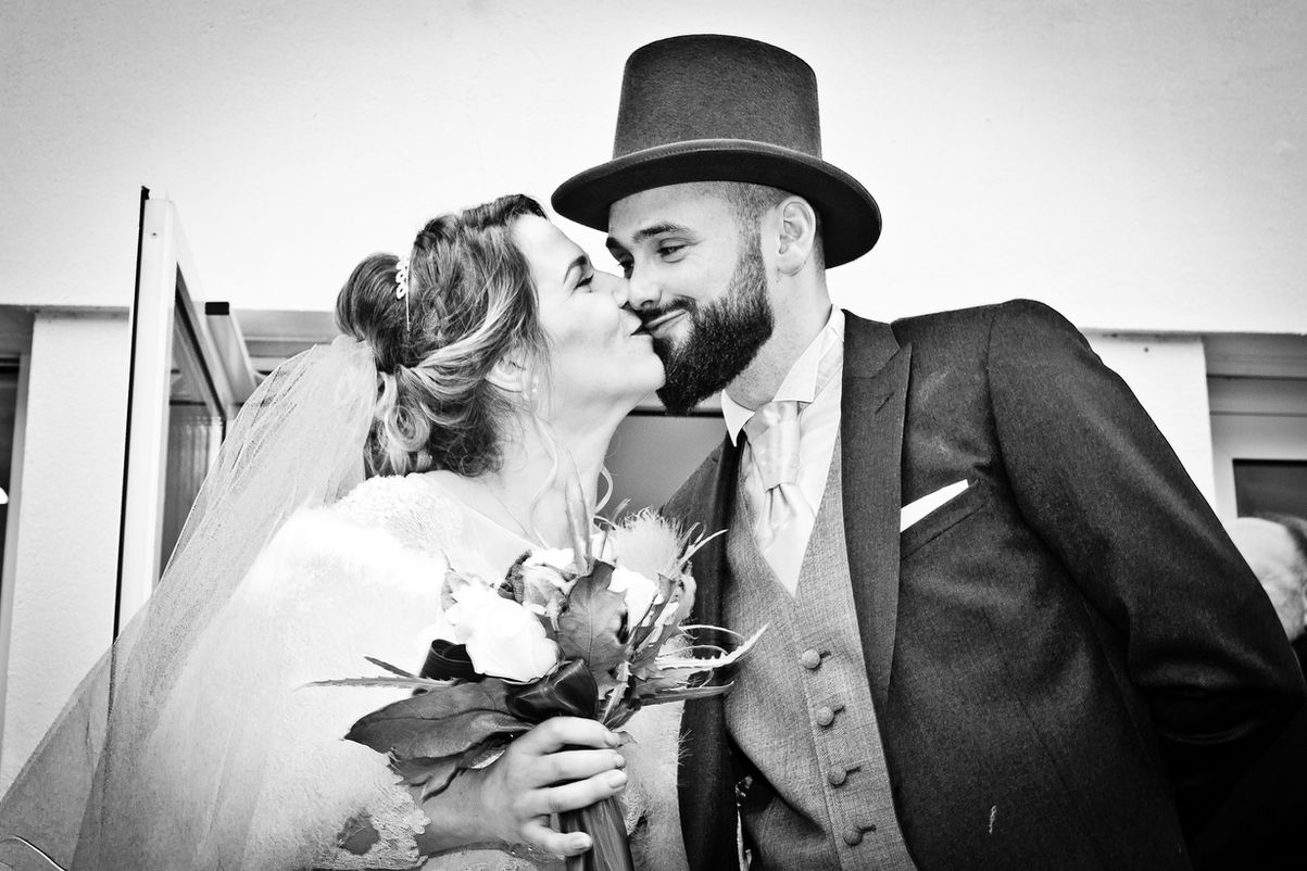 Couple s'embrassant lors d'un mariage, bouquet et chapeau, photographe.