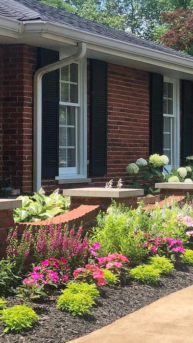 Brick house with colorful garden bed, vibrant flowers, and green hydrangeas.