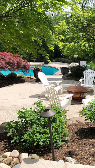 Outdoor patio with fire pit, Adirondack chairs, pool, and lush landscaping.