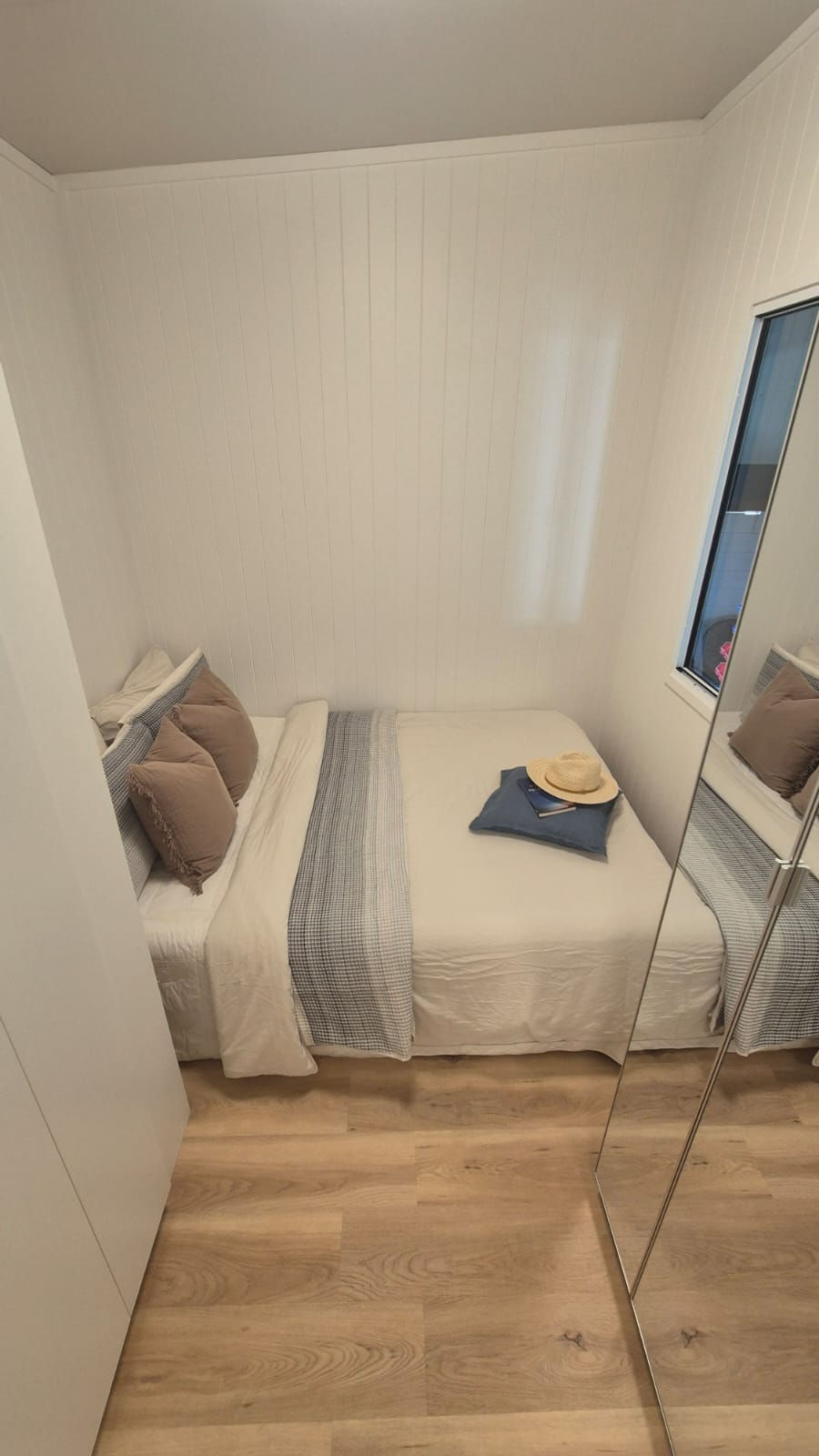 Two-bedroom single story custom tiny home main bedroom, with built-cupboards and window