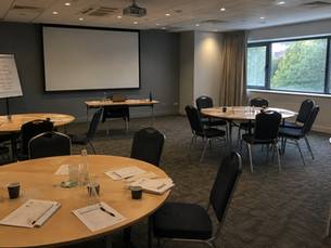 Empty training room after a business simulation workshop with round tables, presentation screen and flipchart.