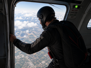 Skydiver standing at the open door of an aircraft preparing to jump into uncertainty.