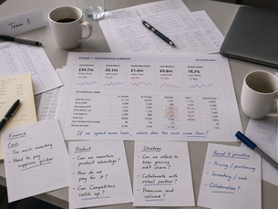 Business simulation performance reports, financial analysis and handwritten notes used by a team to review commercial decisions.