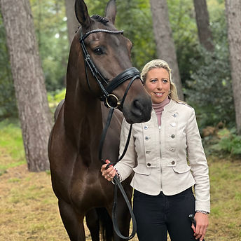 Portrait of Ginny Howe stood next to a dark bay horse wearing a bridle