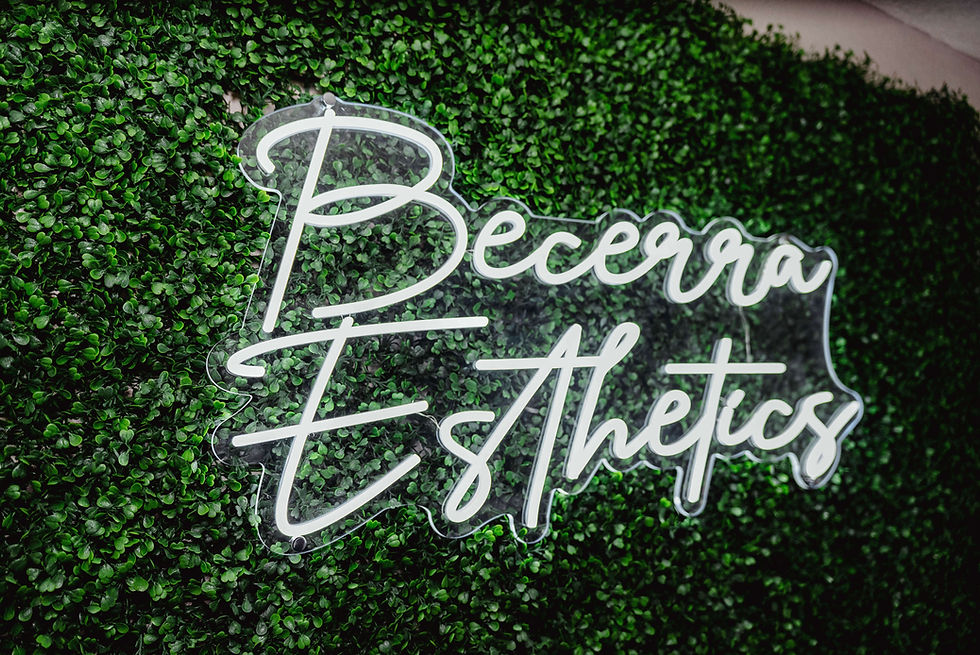 Becerra Esthetics sign mounted on a green foliage wall inside the esthetics studio.