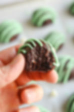 Man holding a Mint Chocolate Chip Protein Balls drizzled with mint chocolate drizzle and a bite taken out of it .