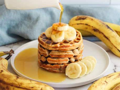 A stack of banana waffles with maple syrup being poured on top.