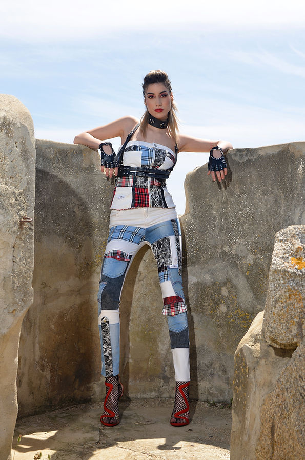 Modella in una tuta con design patchwork distintivo, in piedi tra le rocce, trasmette un’immagine di stile contemporaneo e audace, rappresentando la filosofia anticonformista del brand.