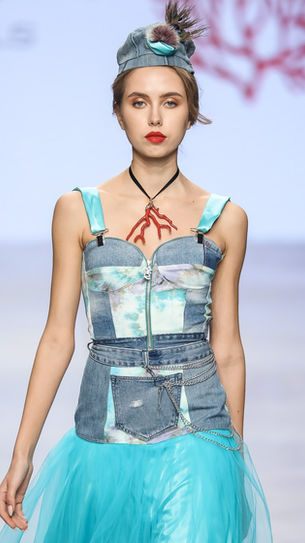 Giovane modella con un look vivace, indossando un vestito blu con dettagli in denim e tulle, che evidenzia la creatività della collezione di Marita Balàzs.