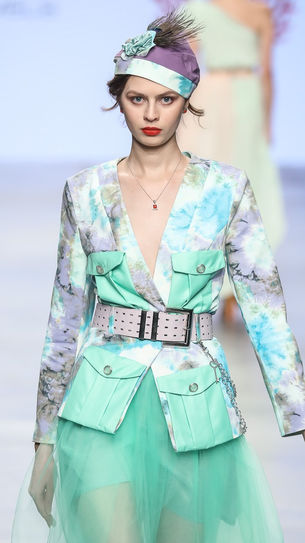 Modella che sfila alla Fashion Week indossando un abito trasparente in tulle verde e una giacca elegante, esprimendo un’eleganza fresca e contemporanea.