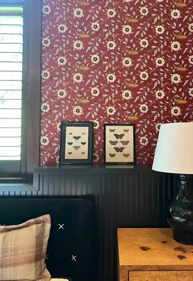 Charcoal fluted wainscoating with crimson floral wallpaper, butterfly print frames and dark ceramic lamp in luxury vignette
