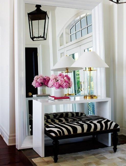 Elegant entryway with zebra print bench, white console table, pink peonies, & arched window.