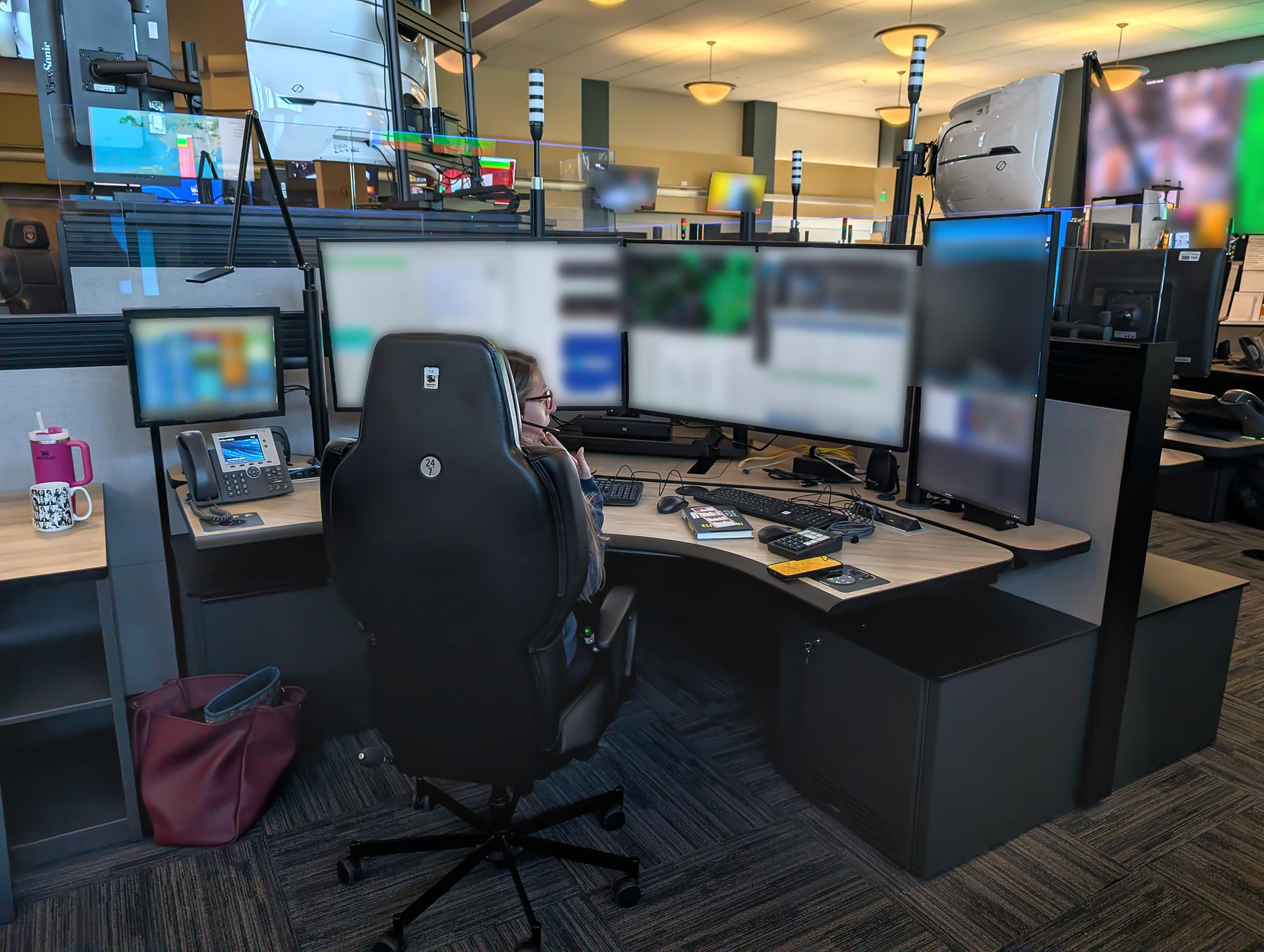 911 dispatcher working comfortably during Telecommunicators Week at a control room workstation, highlighting stacked monitors with both rows of bezels positioned at eye level to prevent neck strain
