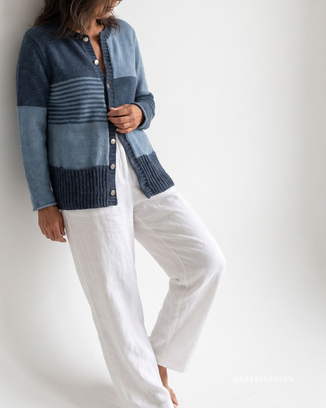 Frontansicht der gestrickten Jeans Jacke in verschiedenen Blautönen mit Knopfleiste, Streifenbereich und weißem Outfit.