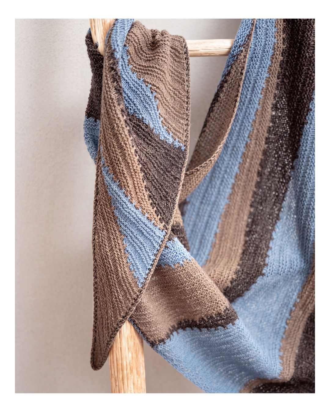 Asymmetrisches TJELLE Dreieckstuch mit blau-braunen Streifen auf einer Holzleiter