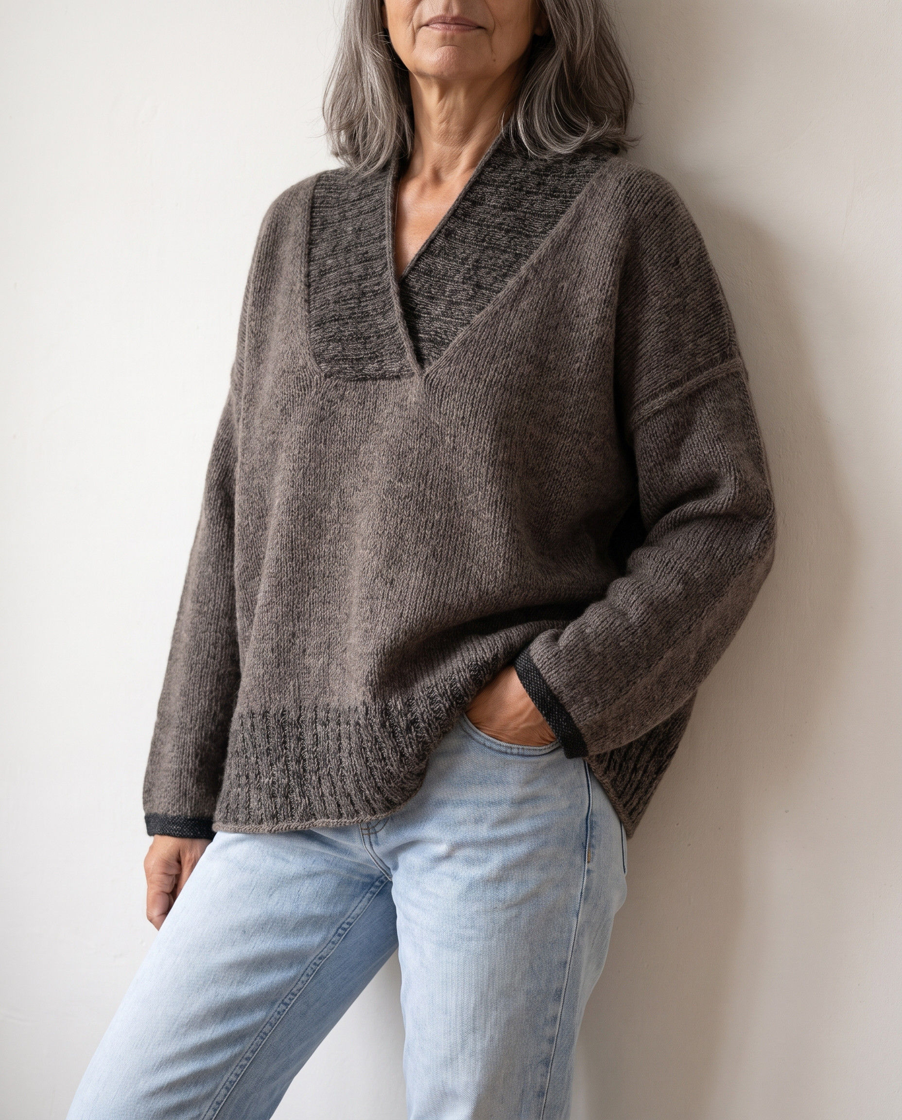 ASHLINE Sweater in graubrauner Melange mit tiefem V-Ausschnitt und überschnittenen Schultern in seitlicher Studioansicht.