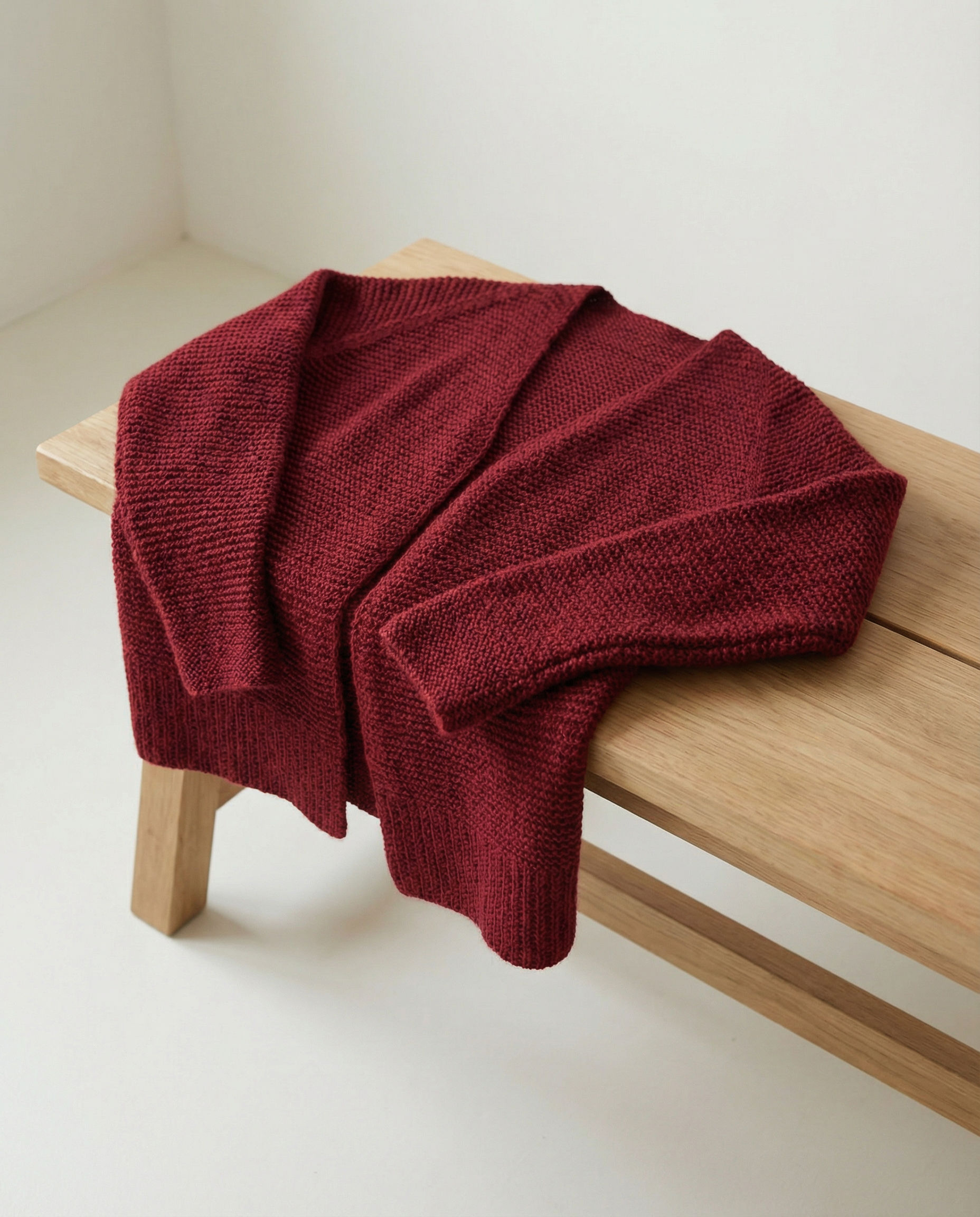 Kraus rechts gestrickte Strickjacke „Schlichte Jacke“ von Safridesign, liegend auf heller Holzbank